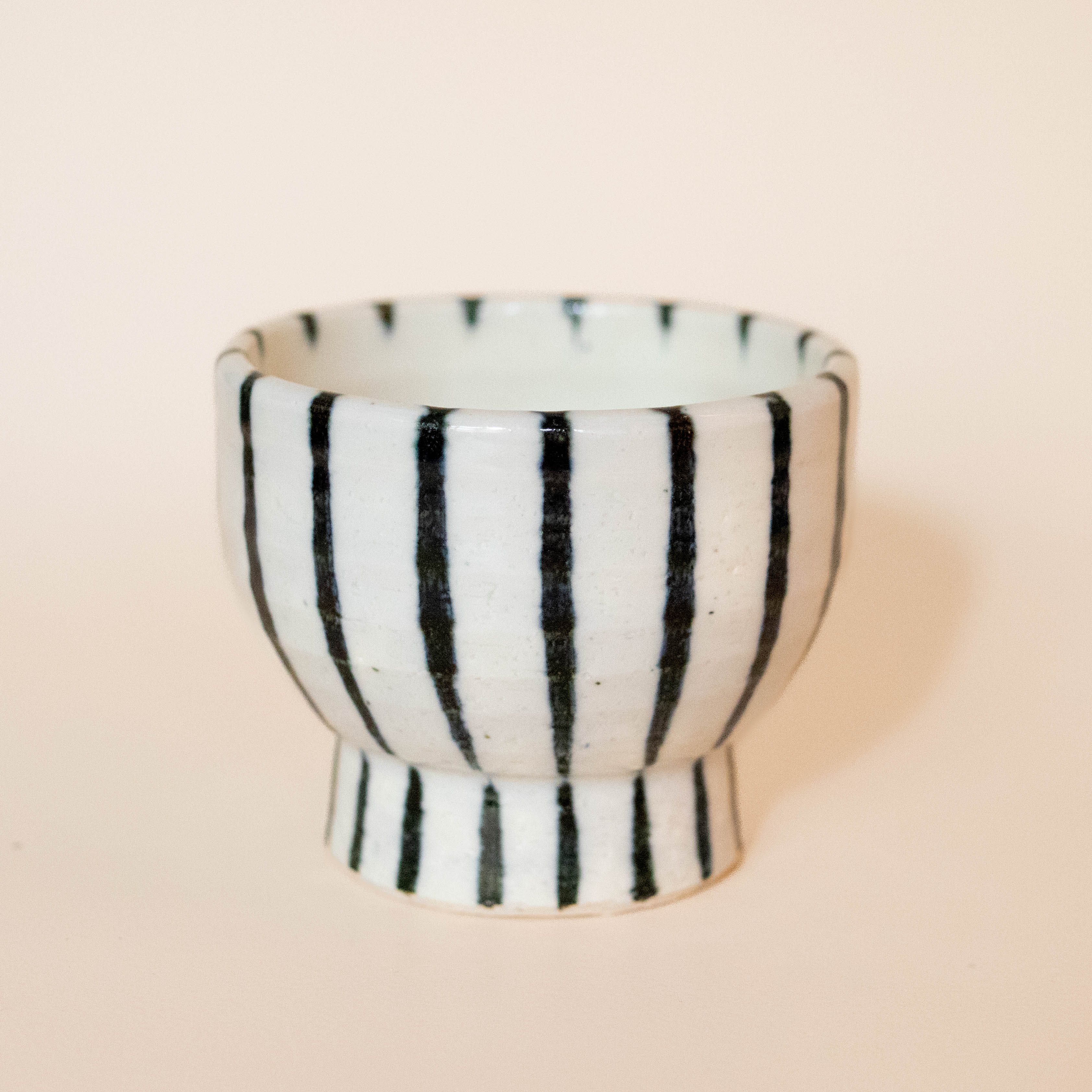 White ceramic cup on foot with dark blue stripes