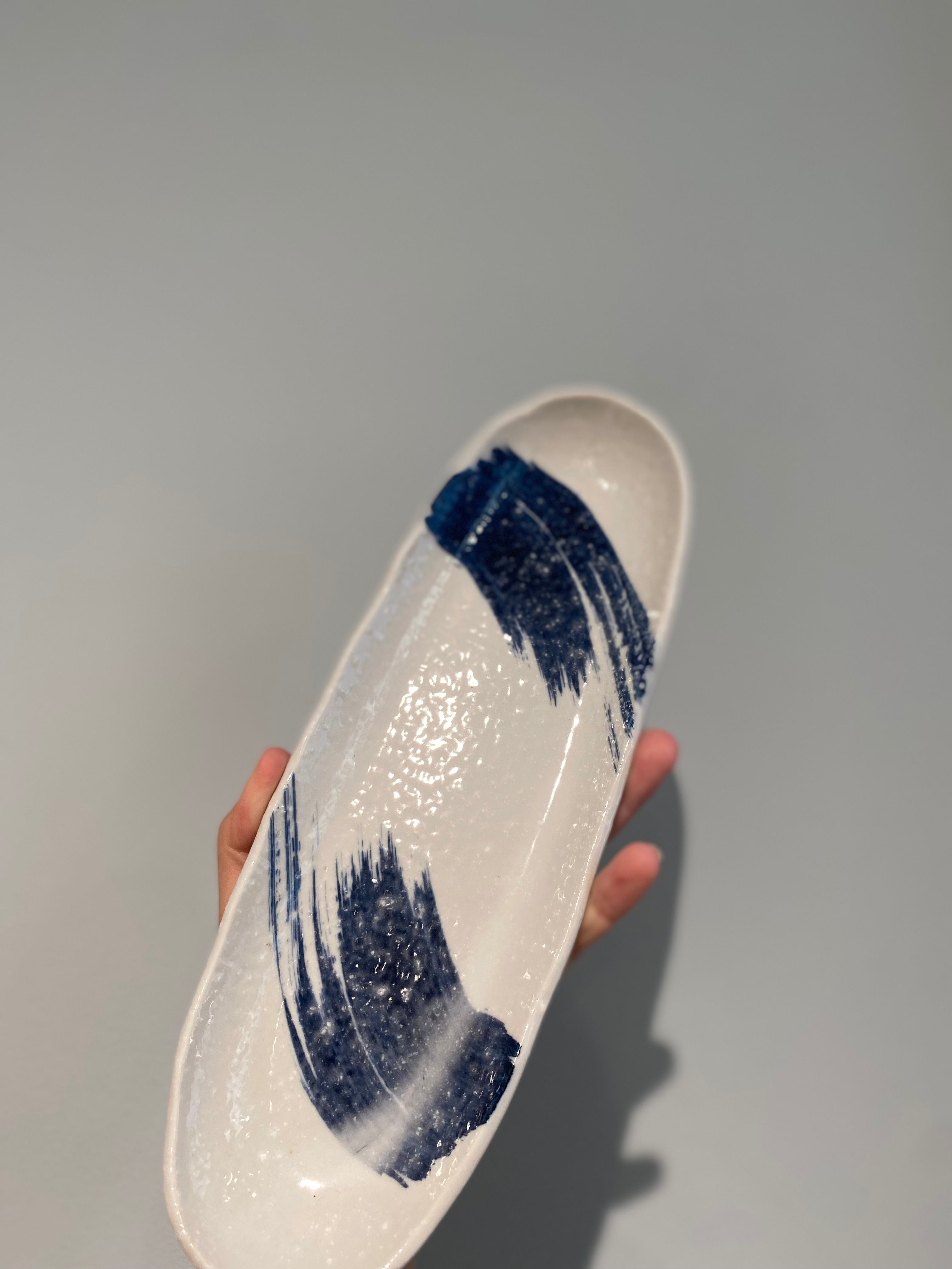 Elongated sushi dish with white glaze and blue brush strokes