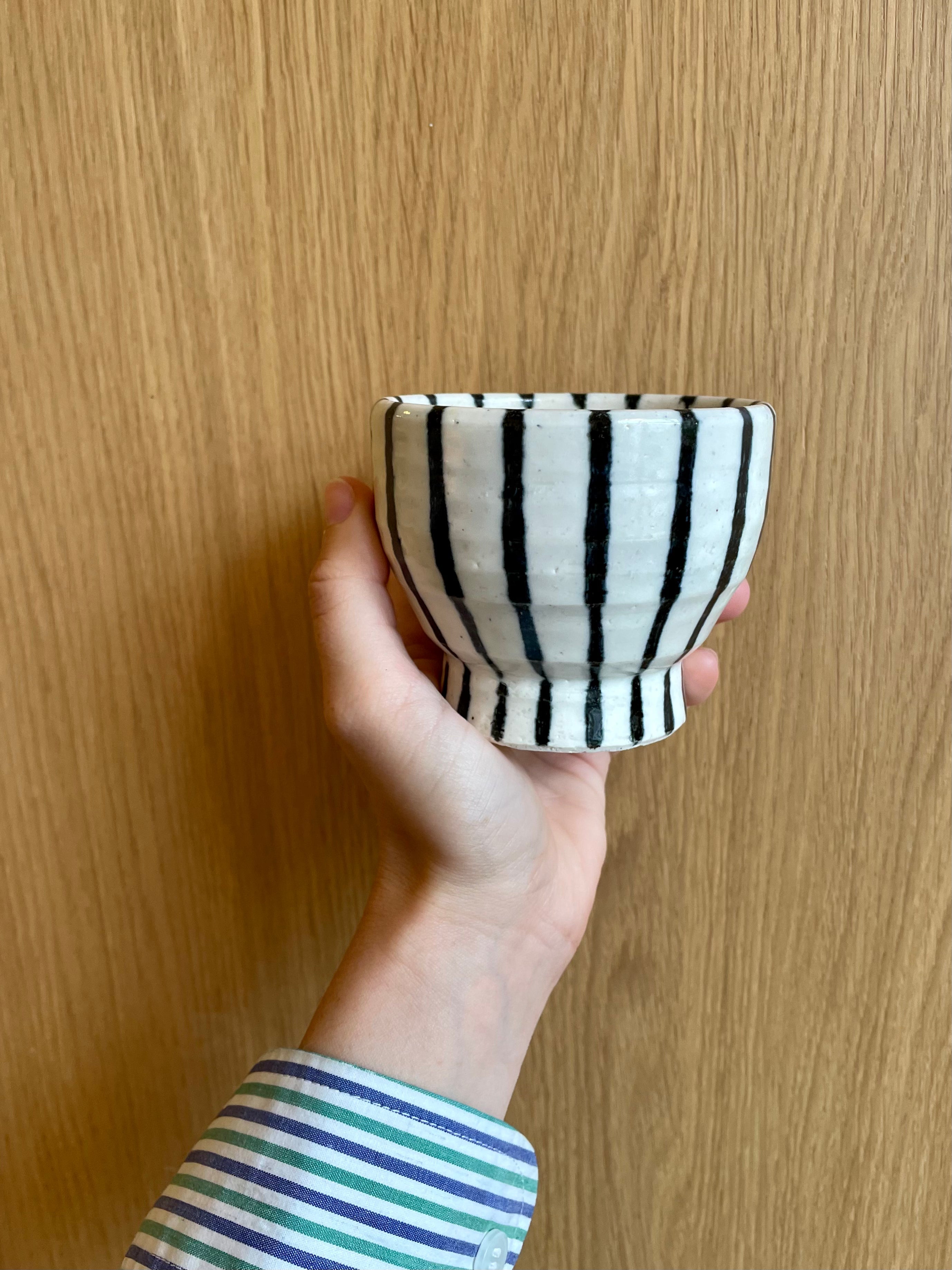 White ceramic cup on foot with dark blue stripes