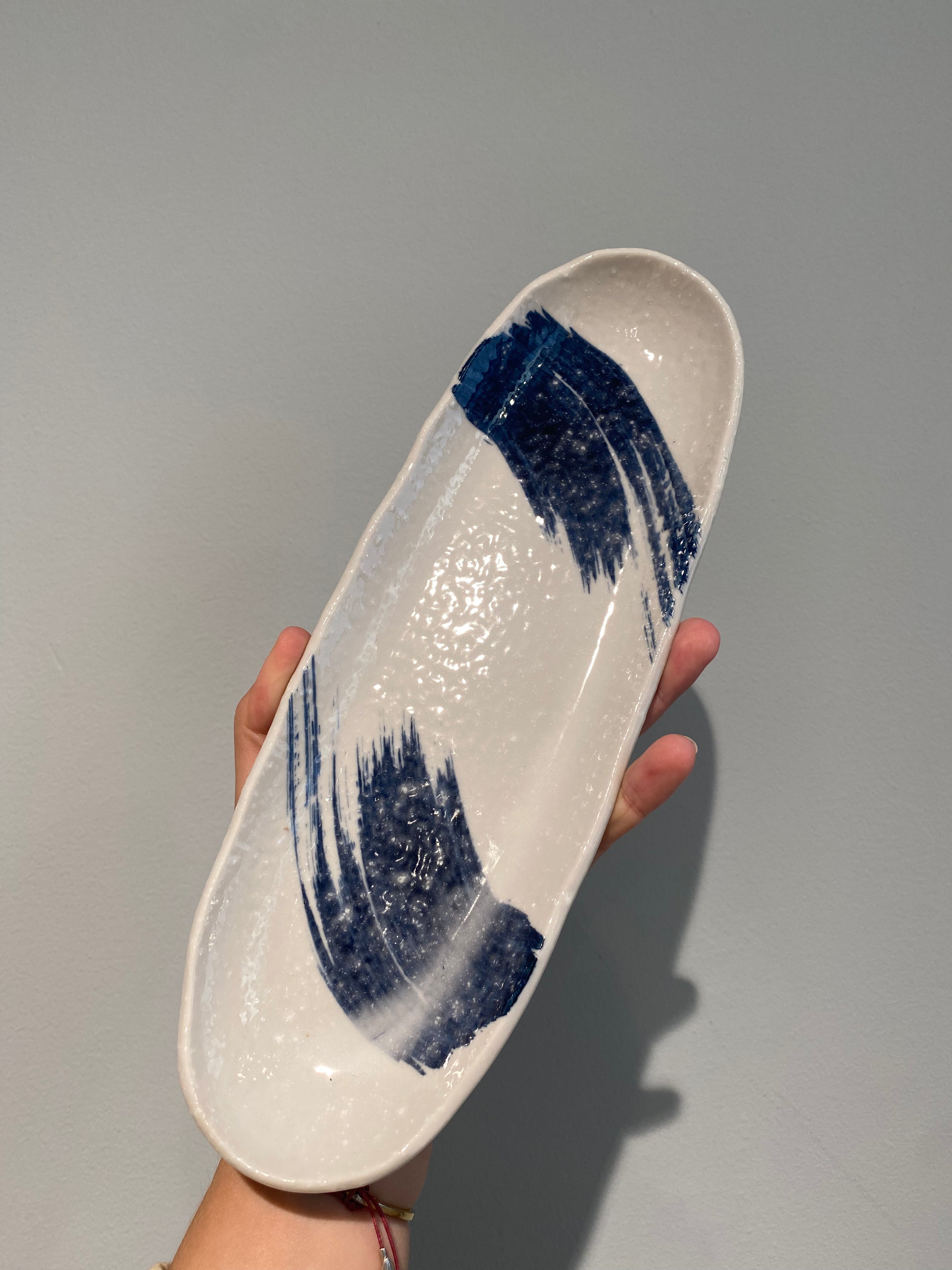 Elongated sushi dish with white glaze and blue brush strokes