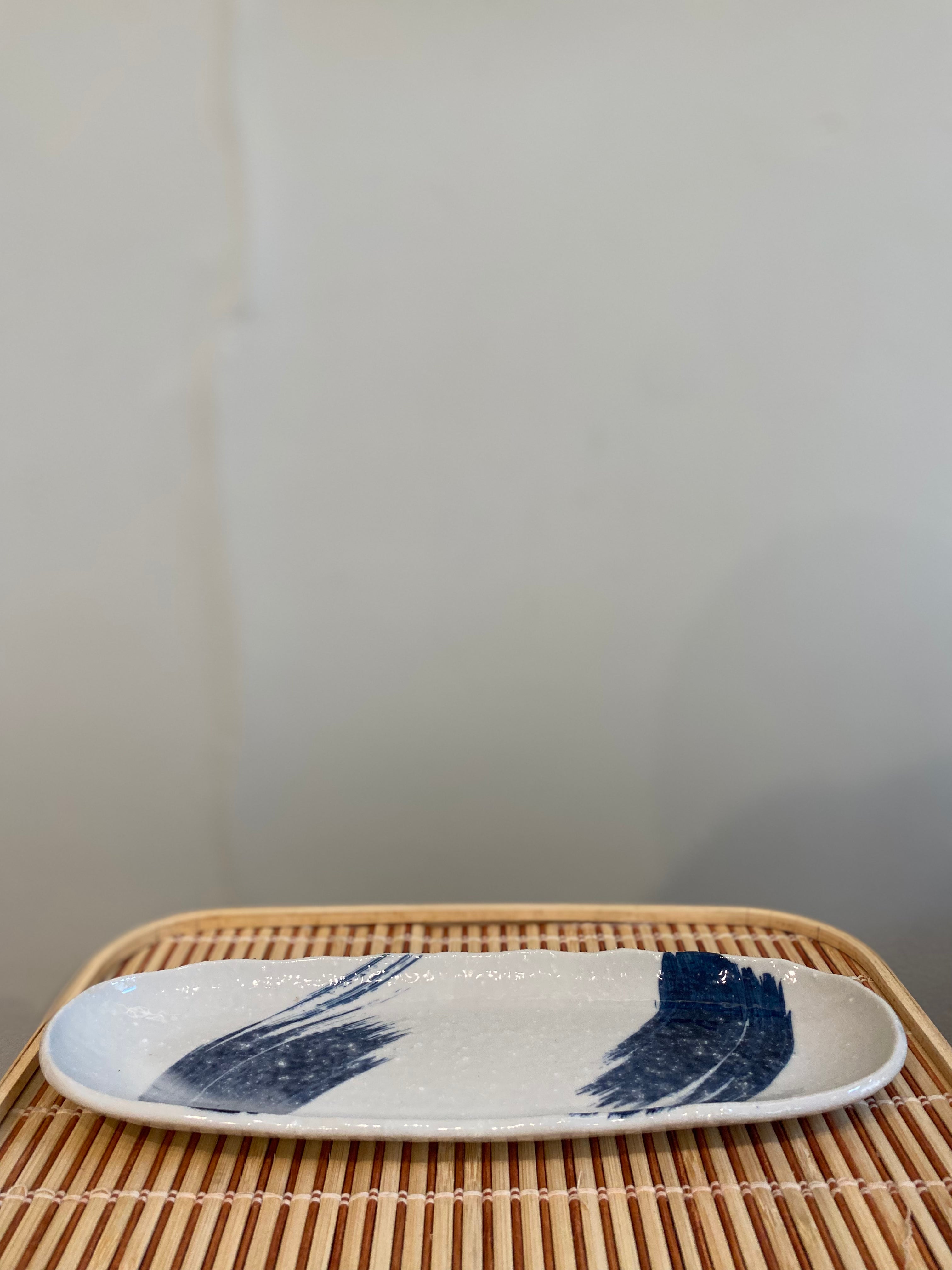 Elongated sushi dish with white glaze and blue brush strokes